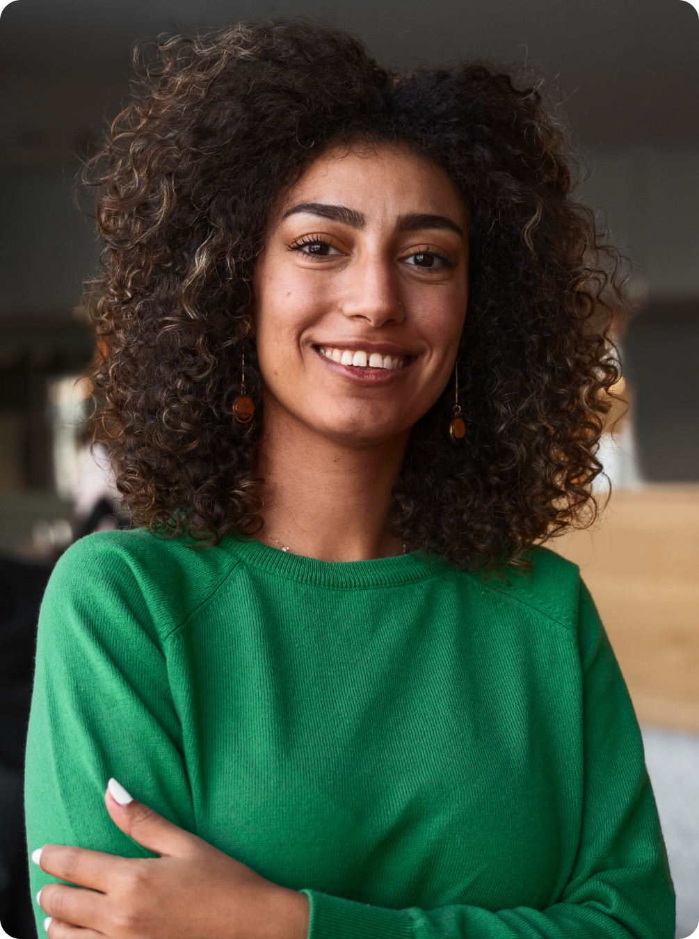 A professional woman with curly hair wearing a green sweater with arms crossed.